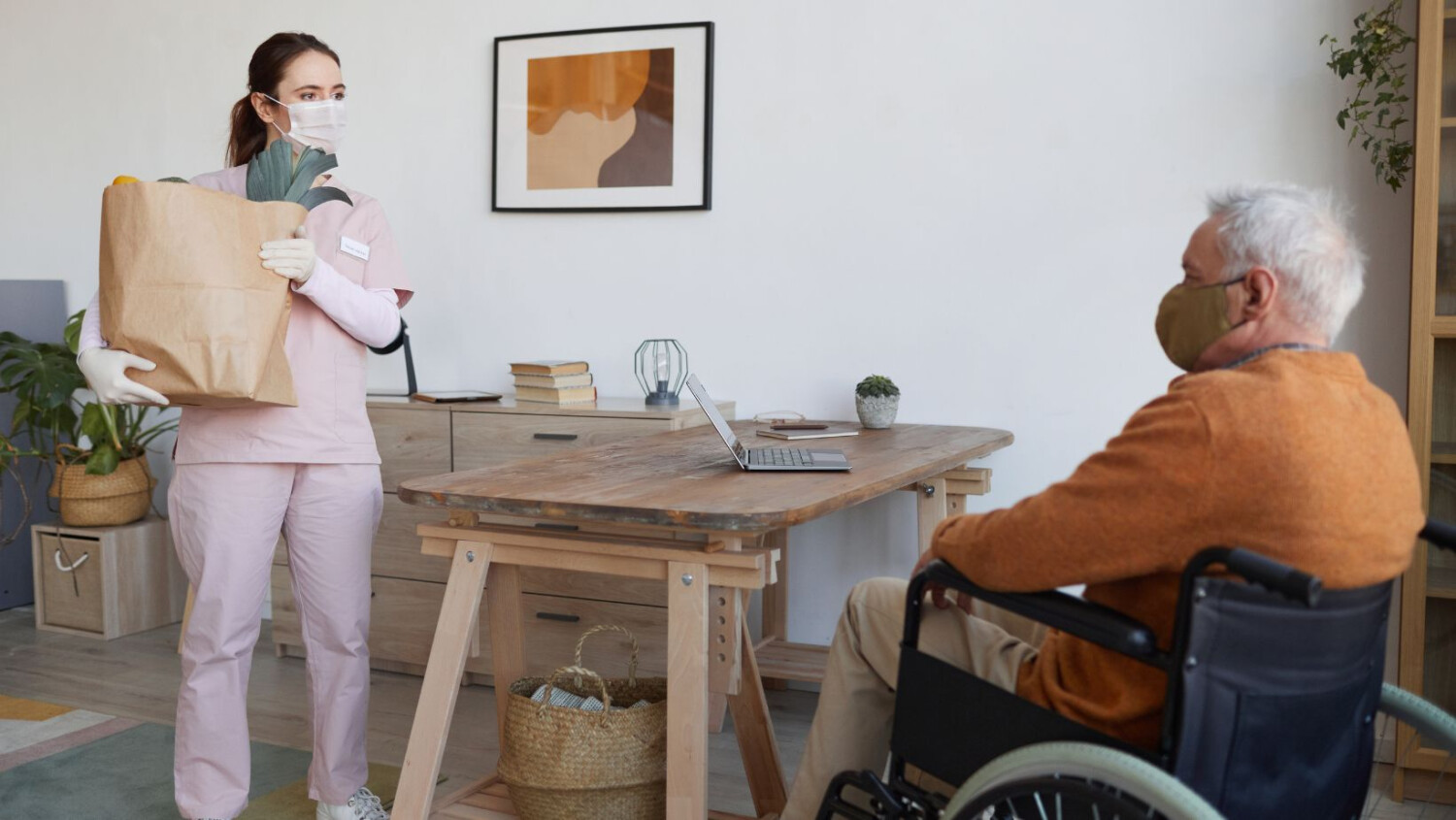 woman-caregiver-holds-grocery-bag-man-in-wheelchair